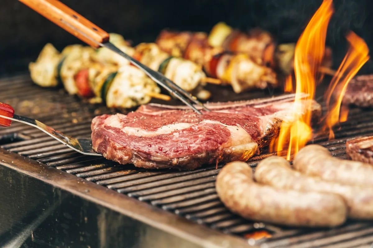 Carne e linguiça grelhando na churrasqueira a gás — botijão P5 portátil para churrasco em Campo Grande