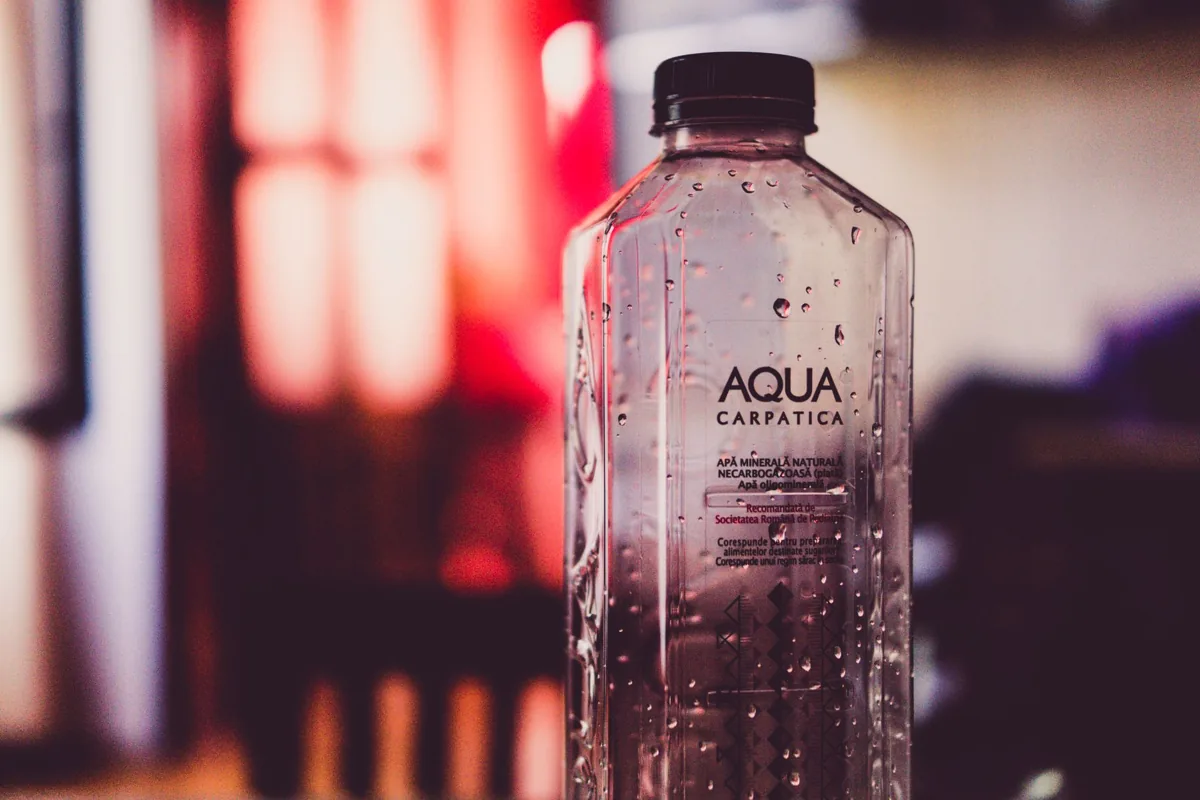 Detailed view of an Aqua Carpatica water bottle with droplets and blurred background.