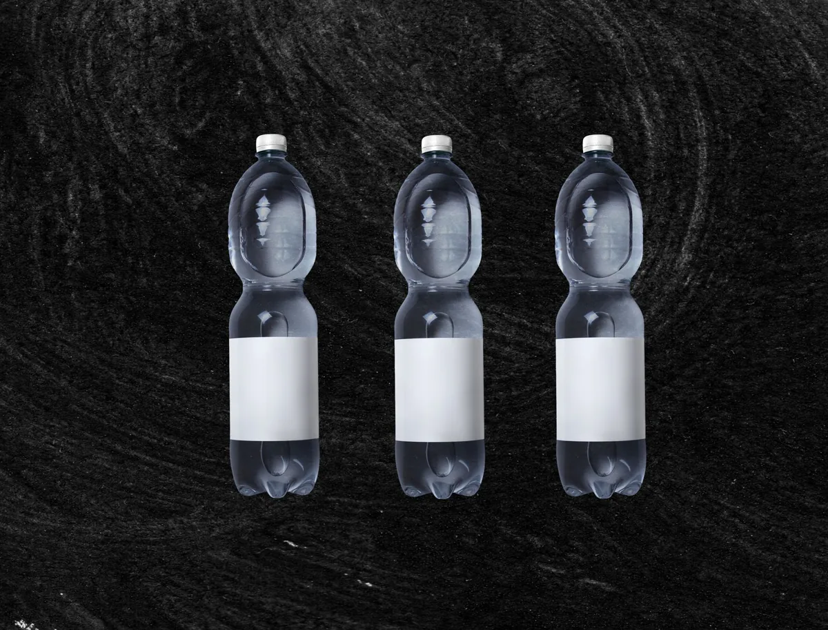 Plastic bottles of still spring water with white blank sticker placed against rough black background