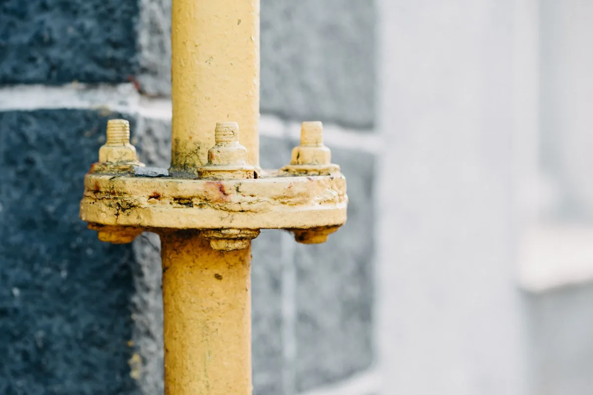 Detailed view of a rusty yellow gas pipe against a textured wall.