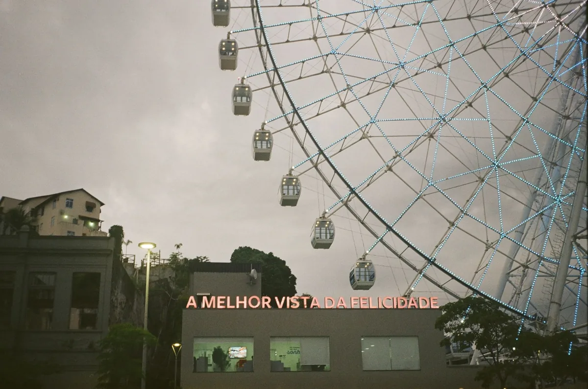 From below of Ferris wheel with cabins and modern buildings against cloudless sky
