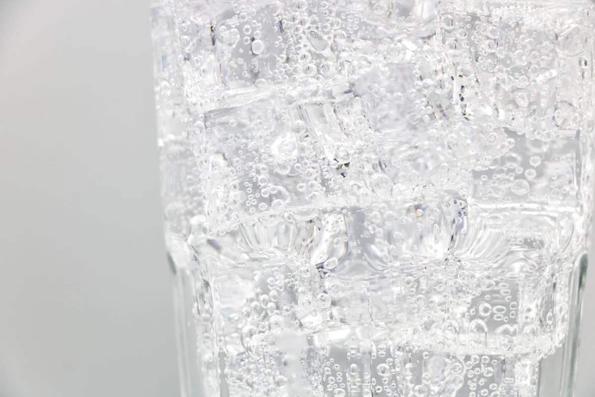 Refreshing sparkling water with ice cubes in a clear glass, close-up view.